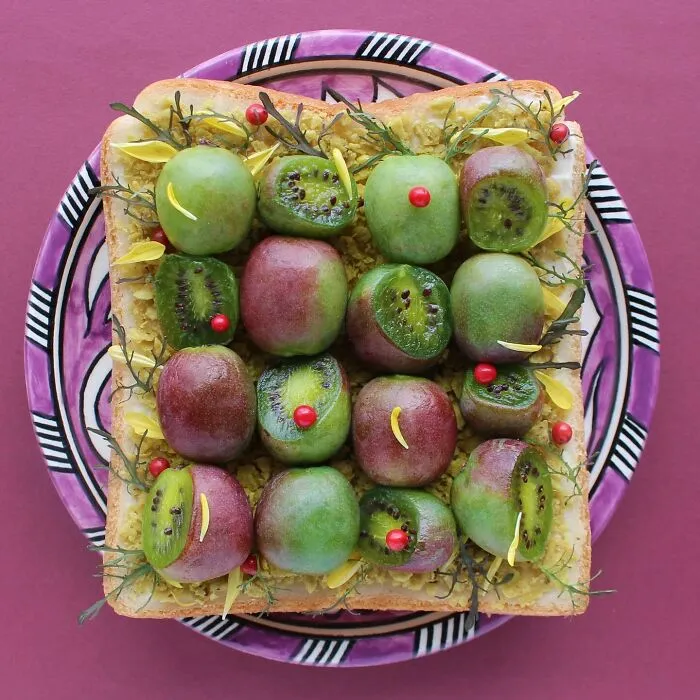 Creative toast design featuring green and purple fruits with yellow petals on a patterned purple plate.