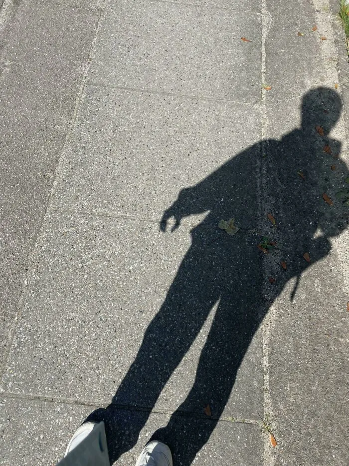 Shadow of a person on a sidewalk, wearing sneakers, capturing a completely unremarkable photo with entertaining elements.