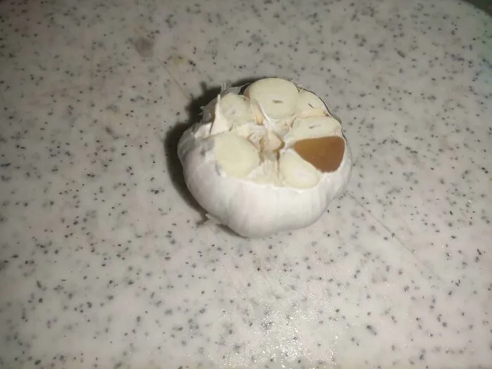 Garlic bulb with one brown clove on a speckled countertop, an unremarkable photo with entertaining qualities.