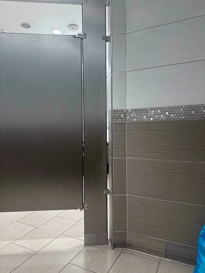 Partial view of a public restroom stall door and tiled floor capturing everyday life in the US through American eyes.