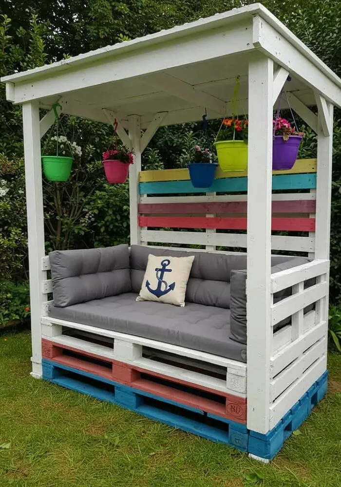 Outdoor wooden pallet sofa with colorful cushions and hanging flower pots, showcasing creative woodworking ideas.