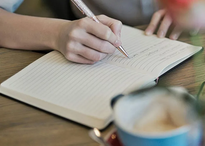 Person writing in a journal, reflecting on heartbroken stories and signs of significant others cheating in a cozy setting.