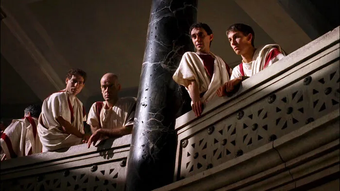 Characters in a historical setting on a balcony, dressed in period costumes, depicting a visually engaging scene from a TV show.