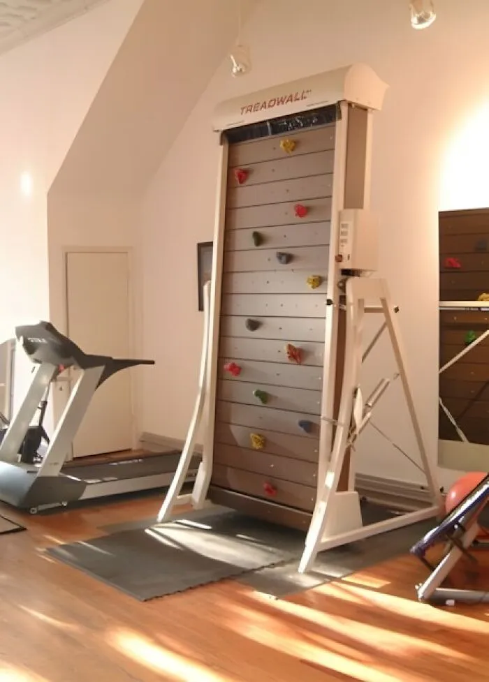 Indoor climbing wall made of wood with colorful grips in a bright room featuring other workout equipment woodworking ideas