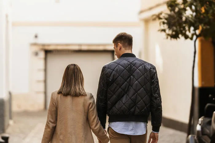 A woman and a man walking hand-in-hand down a street, highlighting differences in dating experiences.