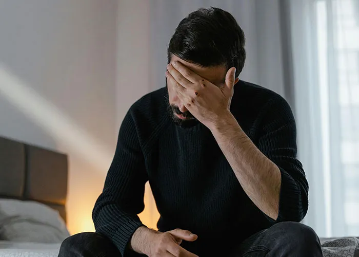 Man sitting on bed with hand on face, showing heartbroken emotion after realizing significant other was cheating.