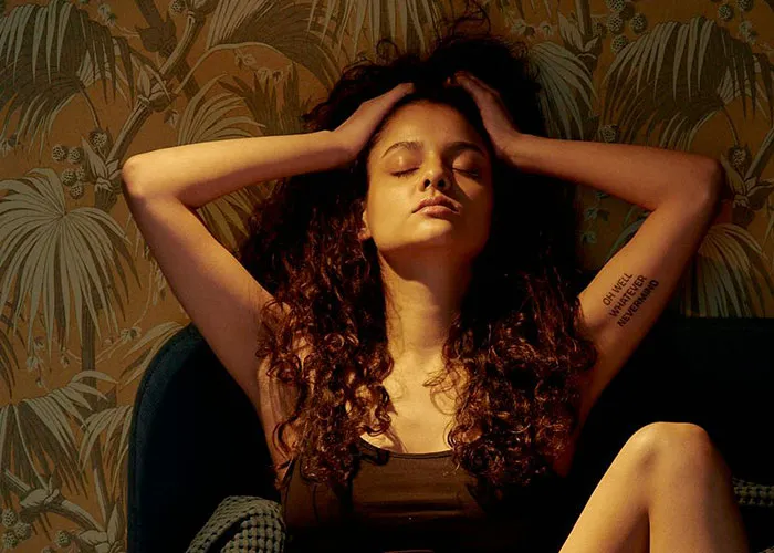 Woman with curly hair sitting with eyes closed, appearing heartbroken, reflecting on cheating in a relationship.