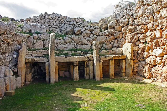 Ancient man-made stone structure with large vertical pillars and a circular surrounding wall under a cloudy sky.