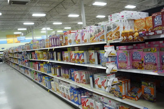 Grocery store aisle with shelves stocked with various restaurant food cereals and breakfast products in boxes and cartons.