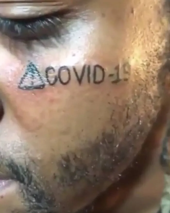 Tatuaje facial con texto COVID-19 y símbolo, ejemplo de tatuajes horribles que muchas personas no reconocen como malos.