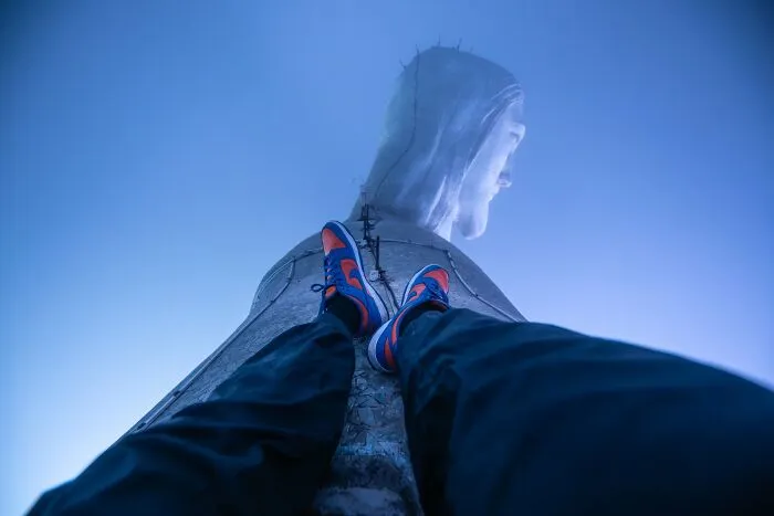 Vista desde abajo de persona con zapatillas sobre estatua gigante, foto curiosa que muestra otra perspectiva.