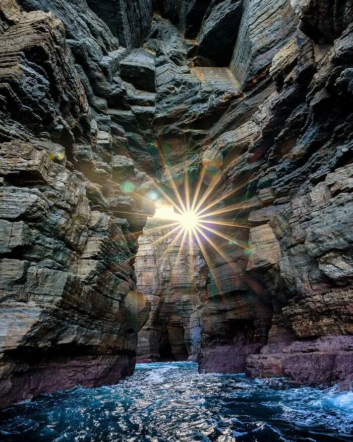 Dramatic oceanic scene with sunlight streaming through rocky cliffs, creating a magical atmosphere where ocean meets sky.