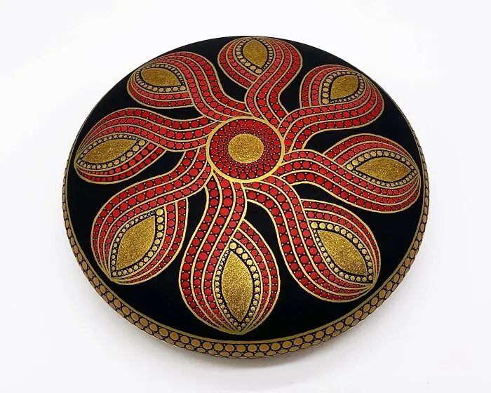 Beautiful mandala art intricately painted on a smooth stone, featuring red and gold swirling patterns.