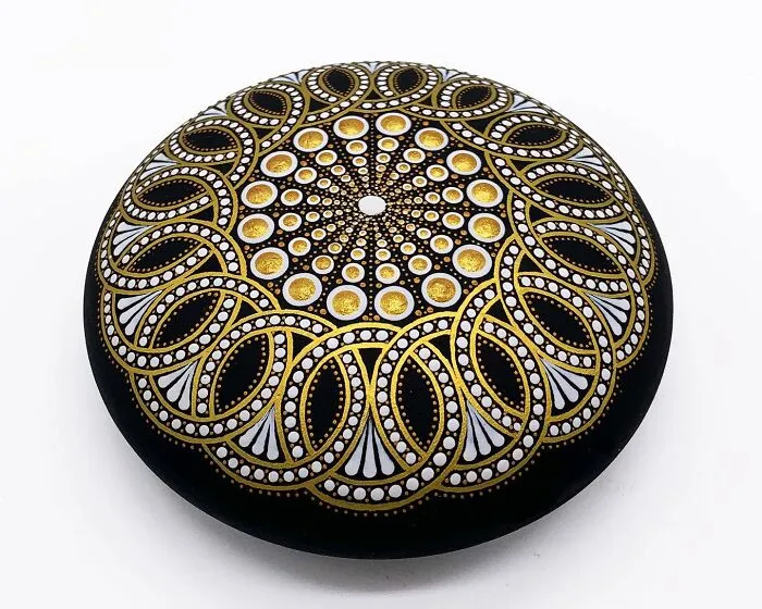 Stone with beautiful mandala art in gold, white, and black patterns.