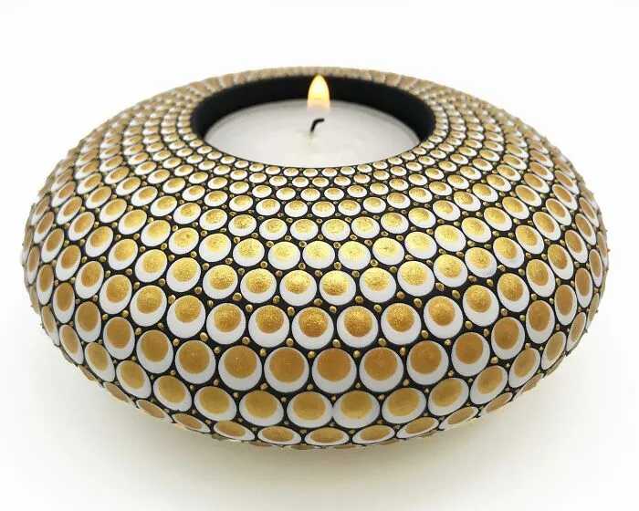 Stone with beautifully painted mandala patterns, featuring intricate gold and white dots, surrounding a lit candle.