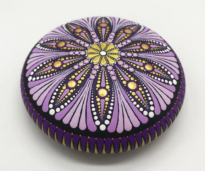 Beautiful mandala artwork on stone with intricate purple, gold, and white patterns.