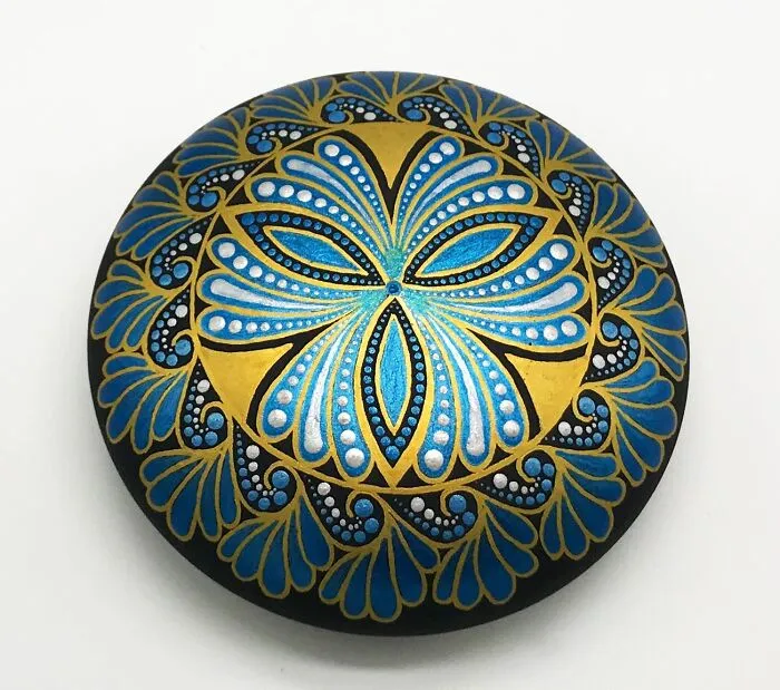 Beautiful mandala art painted on a stone featuring intricate blue and gold patterns.