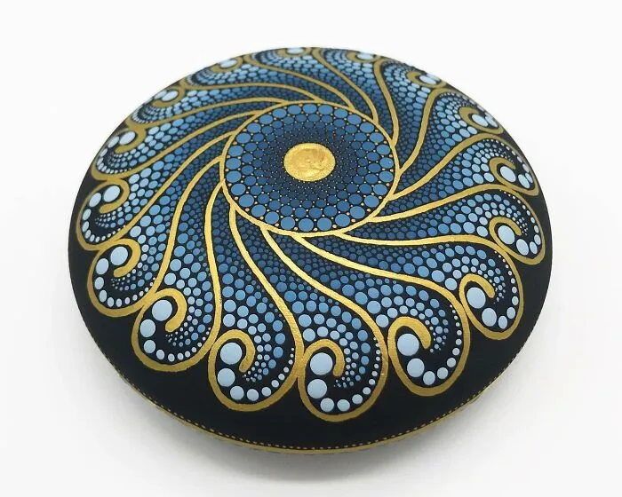 Intricate mandala art on a stone, featuring blue and gold patterns.