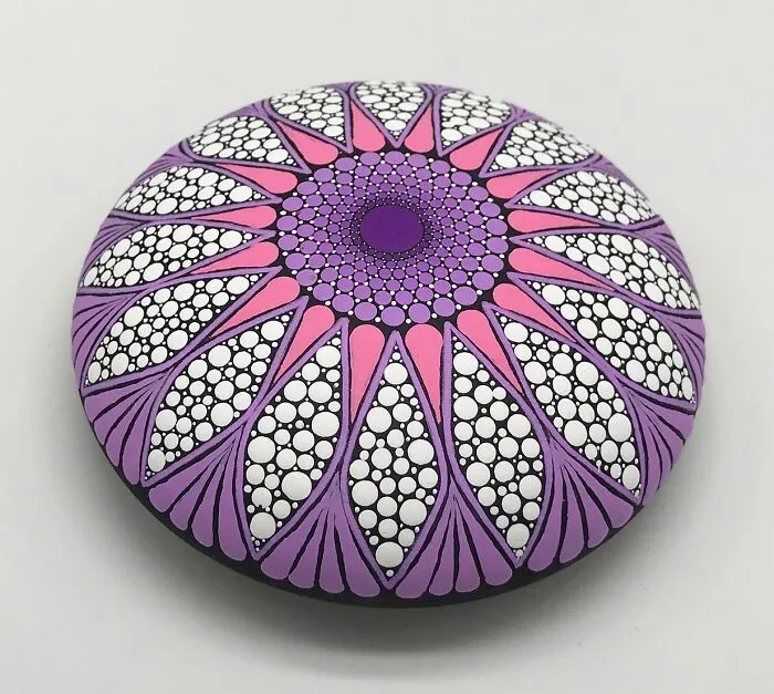 Colorful mandala art painted on a smooth stone, featuring intricate patterns in purple and pink hues.