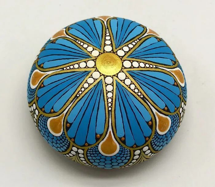Beautifully painted mandala stone, featuring intricate designs in blue, gold, and white.