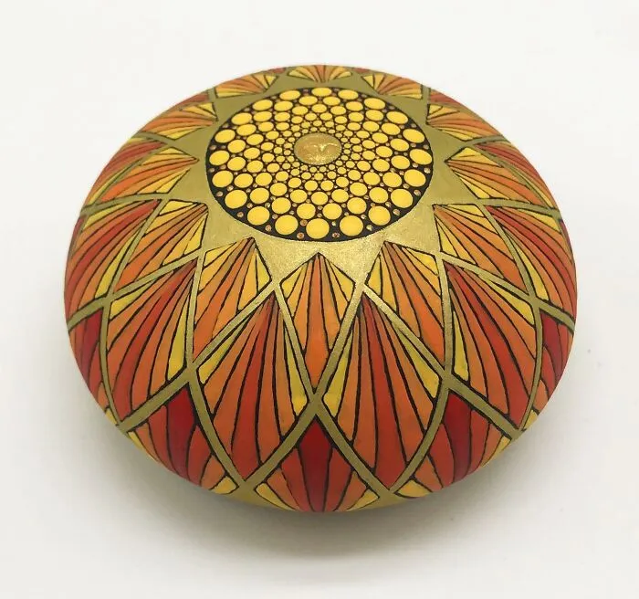 Stone with a beautifully intricate mandala design in orange and yellow hues, showcasing mesmerizing artistry.