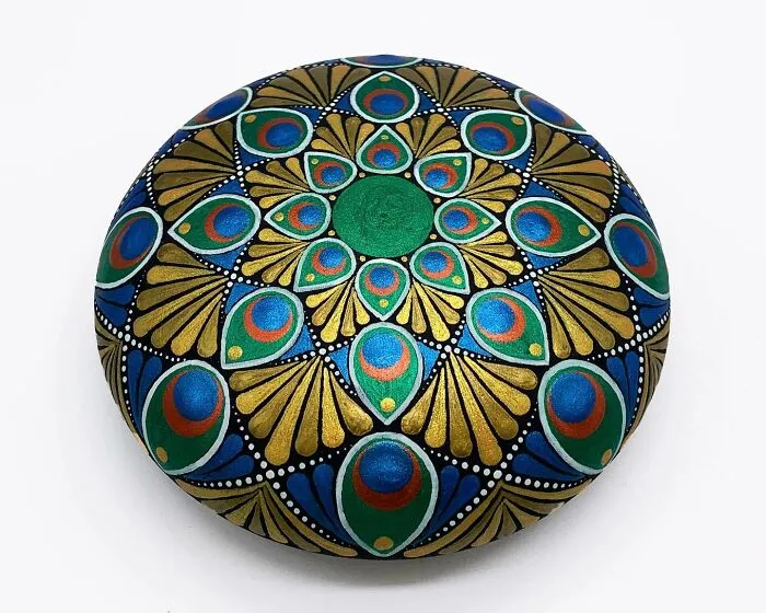 Colorful mandala artwork painted on a stone, featuring intricate patterns in blue, green, and gold tones.