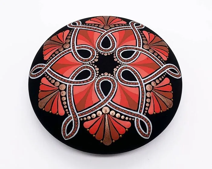 Beautiful mandala art on a stone with intricate red, silver, and bronze patterns.