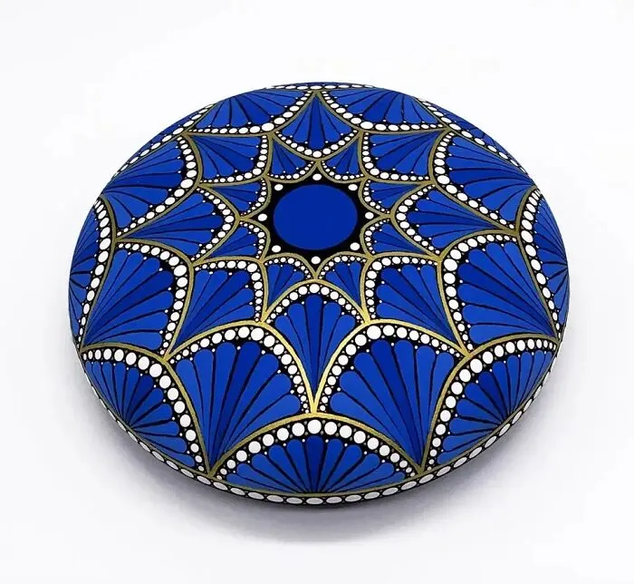 Beautiful mandala art painted on a stone, featuring intricate blue, gold, and white patterns.