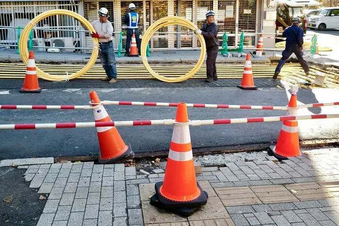 Workers holding large circular pipes, forming a perfect coincidence with orange cones in a construction site.