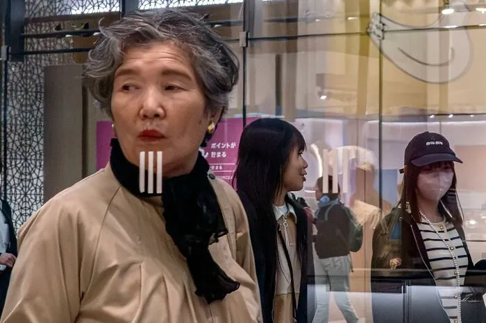 Woman in beige coat coincidentally aligned with glass stripes, creating a lucky visual trick in a public setting.