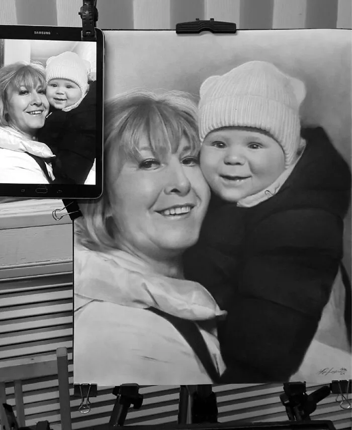 Hyper-realistic pencil portrait of a woman and baby, with reference photo on a tablet next to the artwork.
