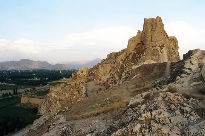 Ancient man-made structure perched on rocky terrain with distant mountains and green fields in the background.