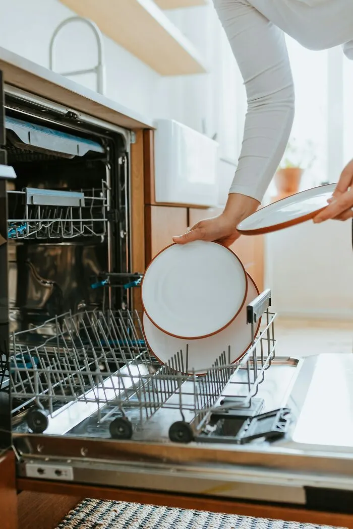 Person loading dishes into a dishwasher, illustrating a cleaning rule.
