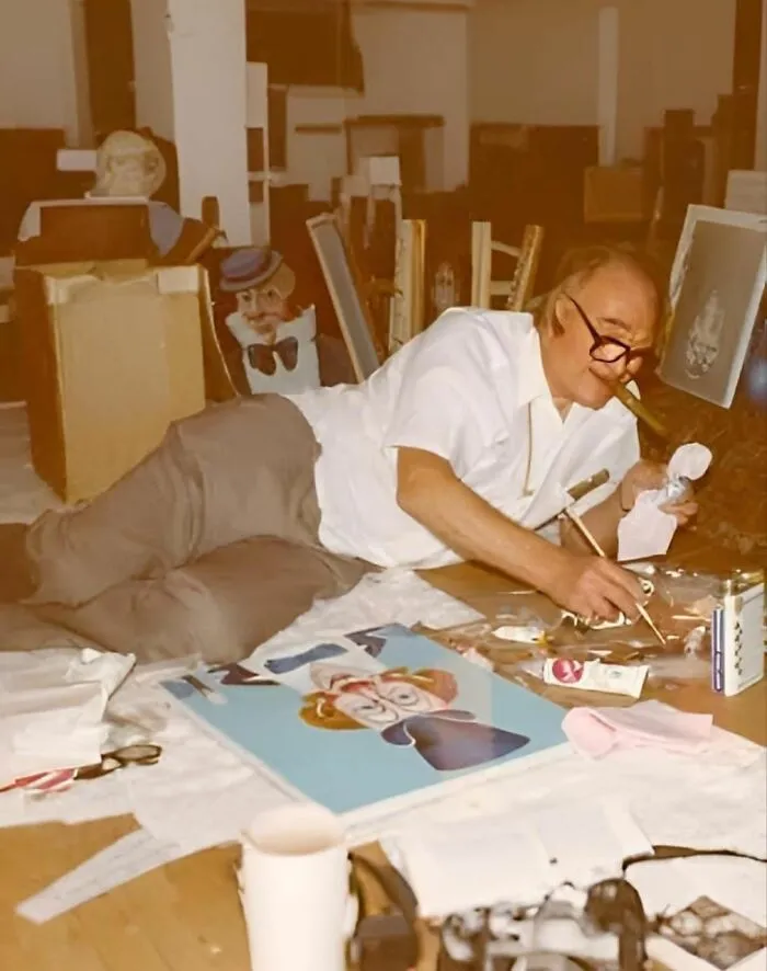 Man painting while smoking a cigar, surrounded by art materials and finished pieces; concept of forbidden stories.