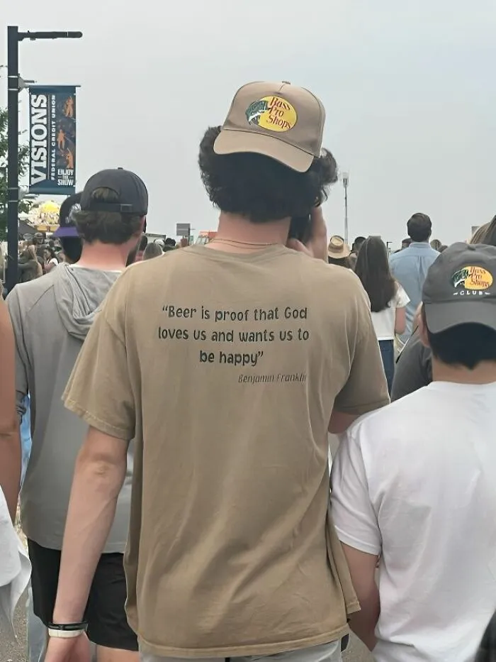 Persona con camiseta divertida y ridícula en público, junto a otras personas en evento al aire libre.