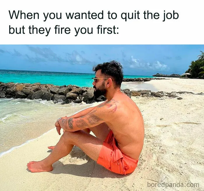 Man in red shorts sitting on a beach, looking at the ocean, capturing funny work meme vibes.