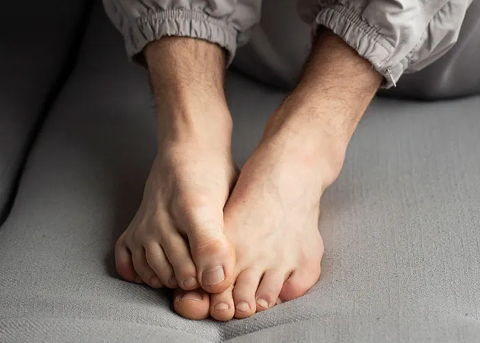 Bare feet on a grey surface, toes slightly curled, wearing light gray pants, hinting at personal discovery in relationships.
