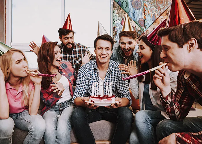 A group of friends celebrating a birthday with hats and noisemakers, featuring a cake with candles.