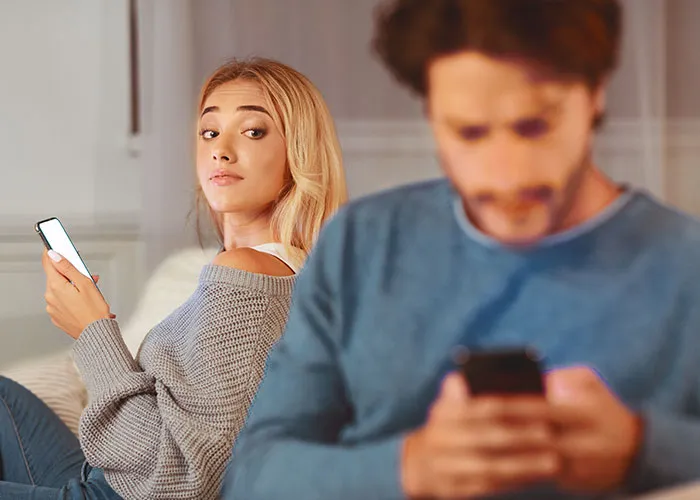 Woman glancing at her partner's phone, hinting at relationship secrets and trust issues.