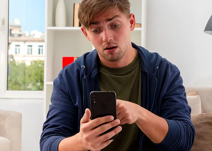 Surprised man in a casual setting looking at a smartphone, discovering unexpected phone contents.