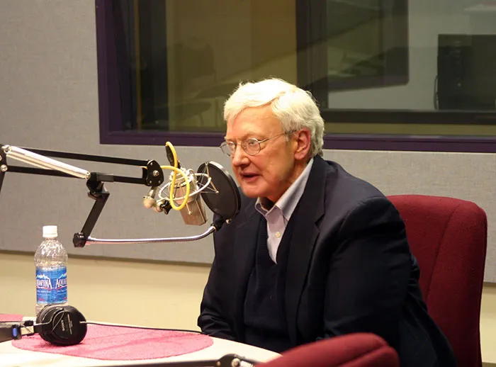 Man in a radio studio speaking into a microphone, wearing glasses and a suit, related to predicting historical events.