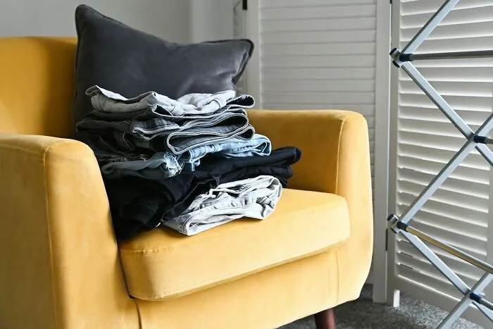 Folded clothes on a yellow chair next to a drying rack, reflecting personal cleaning rules.