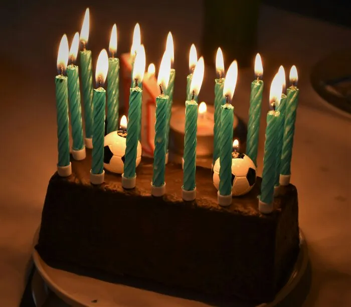 A cake with tall blue candles and small soccer ball decorations resembles a glitch.