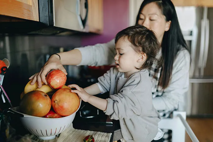 A mother and child reaching for fresh fruit in a kitchen, highlighting family values mothers appreciate about older generations.