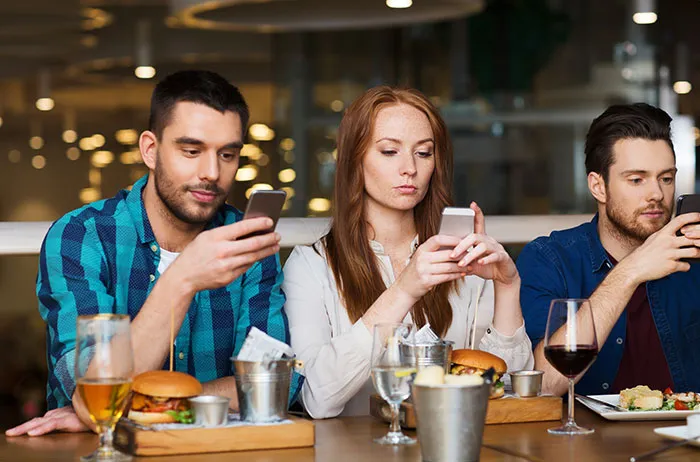 Young people using phones at a table, highlighting a social moment possibly pointing to Boomer insights on technology use.