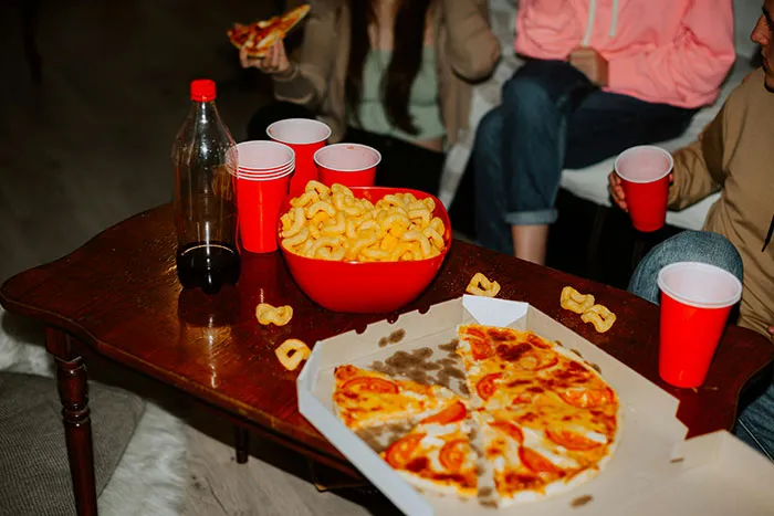 Young people sharing pizza and snacks, discussing what things boomers might be right about, red cups on a table.