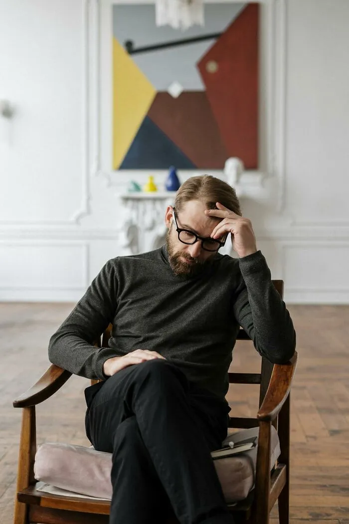 Man with glasses and beard sitting thoughtfully in chair, reflecting on obvious things he has just become aware of