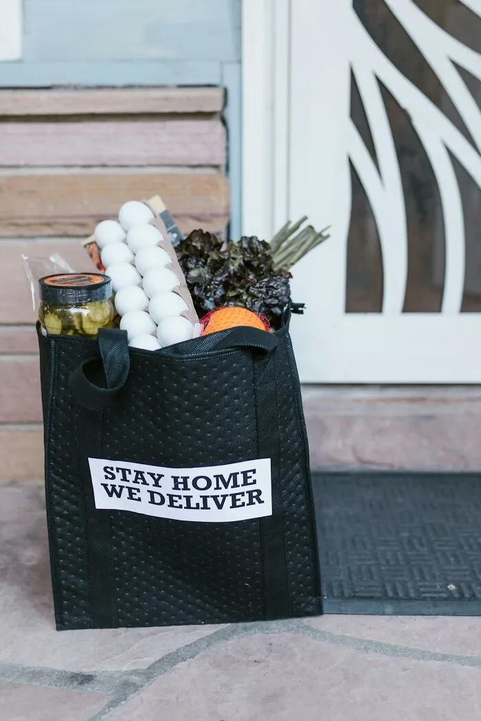 Black grocery bag with eggs, lettuce, and other food items on doorstep promoting restaurant food delivery service.