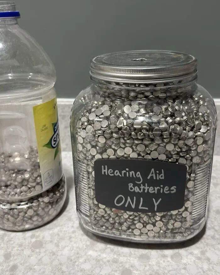 Jar filled with hearing aid batteries labeled "ONLY," alongside a partly filled plastic bottle.