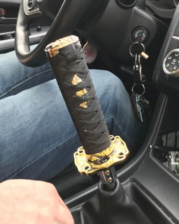 Car interior with a gear shift fashioned like a katana handle, featuring intricate gold and black details.